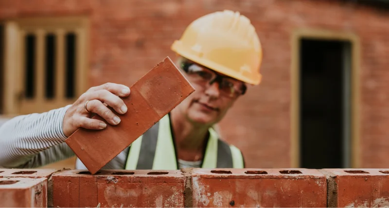 Imagem que ilustra a venda de materiais de construção e acabamentos, com mulher a assentar blocos